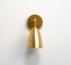 a wall mounted light on the side of a white wall with a gold colored shade