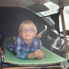 a little boy with glasses sitting in the back of a car seat on a mat