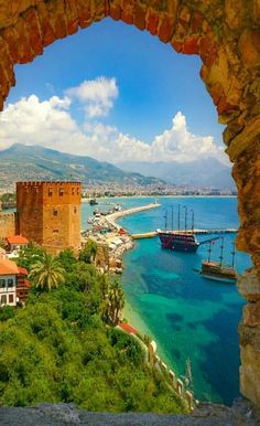 the view from inside an arch looking out at boats in the water and mountains behind