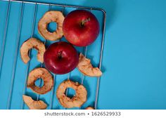 three apples and two donuts on a cooling rack, with one apple half eaten