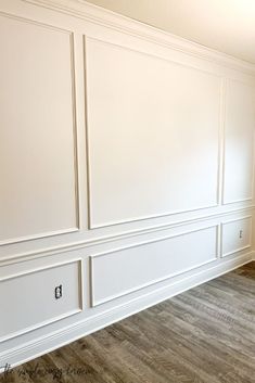 an empty room with white paneling and wood floors