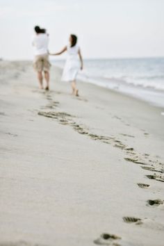 two people walking on the beach holding hands and footprints in the sand as they walk towards the water