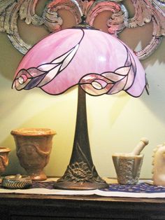 a pink lamp sitting on top of a table next to vases and other items