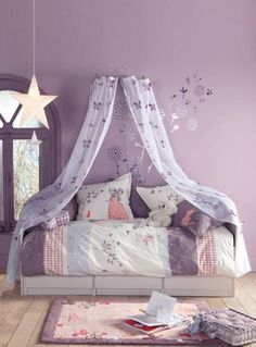 a bedroom with purple walls and white curtains on the canopy bed, rugs and pillows