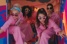 three women in pink outfits and sunglasses are posing for the camera while sitting on a colorful structure