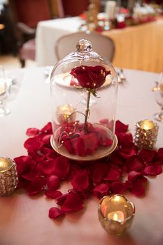 the table is covered with red rose petals and glass clochet, which has been placed on top of it