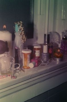 various items are sitting on a shelf in front of a window with candles and bottles