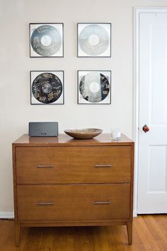 a wooden dresser with three pictures on the wall above it and a laptop computer sitting on top