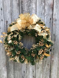 a christmas wreath hanging on the side of a wooden fence with gold bows and berries