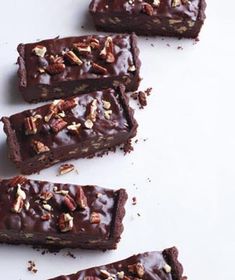 chocolate brownies with pecans on top and one cut in half sitting on a white surface