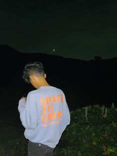 a man standing in the grass at night wearing a sweatshirt with space to grow on it