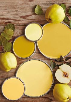 some apples and lemons on a wooden table with yellow paint in the middle, along with two cans of juice