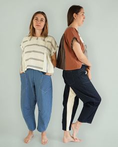 two women standing next to each other in front of a gray wall wearing striped pants