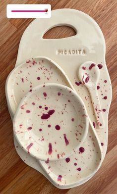 two white dishes with red splatters on them sitting on a wooden floor next to each other