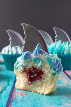 three cupcakes with blue frosting and a shark fin on top