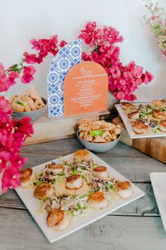 a table topped with plates of food next to pink flowers and an orange sign that reads toon