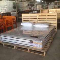 mattresses are stacked on pallets in a large warehouse with wooden tables and chairs