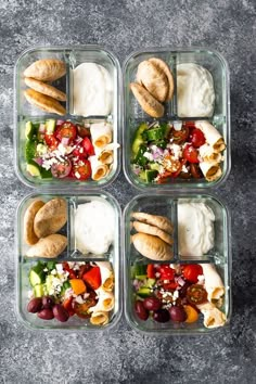 four plastic containers filled with food on top of a gray surface and some breads