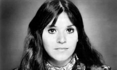 a black and white photo of a woman with long hair wearing a plaid shirt, looking at the camera