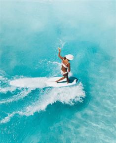 a woman riding a surfboard on top of a wave in the ocean with her arms up