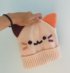 a hand is holding a knitted hat with an orange and brown cat on it