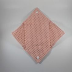 a pink knitted handkerchief folded on top of a white surface with two holes in the middle