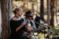 two women singing into microphones and playing guitar in front of an outdoor music stand