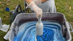 a person in white gloves is pouring blue liquid into a gray container on the grass