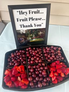 grapes and strawberries are arranged in a tray with a sign that says hey fruit, fruit please thank you