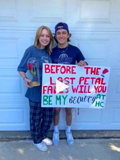 two people standing in front of a garage holding a sign that says before the last petal fall and will you be my beauty