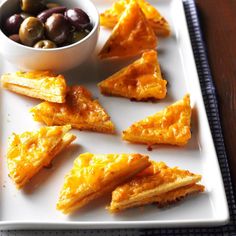 several pieces of food on a white plate with olives in a bowl next to it