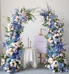 a blue and white wedding arch with flowers on the side, next to an easel