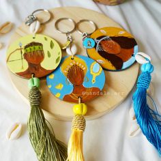 three keychains with tassels on them sitting on a wooden tray next to other items