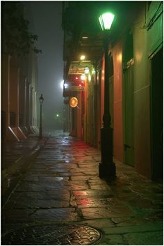 an empty city street at night in the rain with lights shining on buildings and lampposts