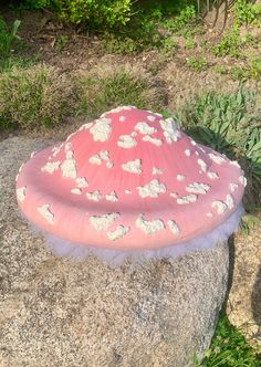 a pink and white umbrella sitting on top of a rock in front of some bushes