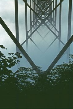 the reflection of trees in water is seen through an iron bridge's railings