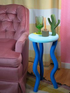 a pink chair sitting next to a table with a glass on it and a cactus