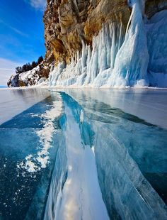 the water is crystal blue and there are ice formations on the side of the mountain