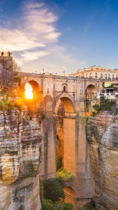 the sun is setting on an old bridge over a canyon in europe with cliffs and buildings