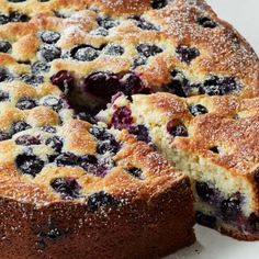 a cake with blueberries and powdered sugar is cut from the top to show it's filling