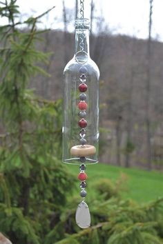 a glass bottle with beads hanging from it's side in front of some trees