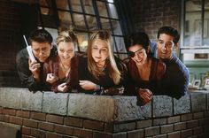 four people looking at their cell phones while leaning on a brick wall in a kitchen