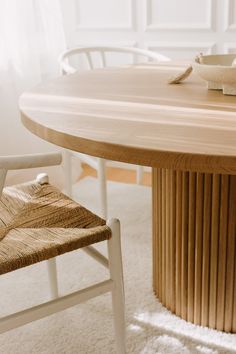 a wooden table with two chairs and a bowl on it's end, in front of a window