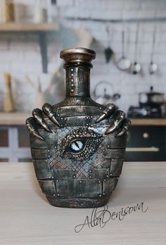 a metal vase sitting on top of a wooden table next to a kitchen counter with an eye in it