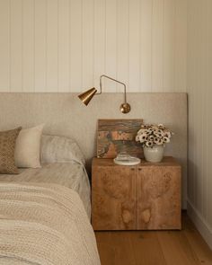 a bed room with a neatly made bed next to a night stand and flower vase