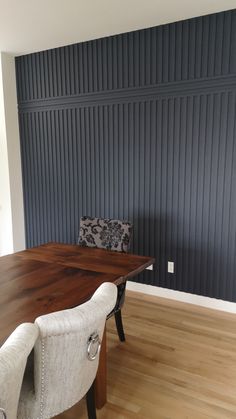 a dining room table with two chairs and a bench in front of a striped wall