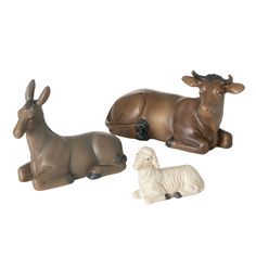 three ceramic animals sitting next to each other on a white surface with one laying down and the other lying down