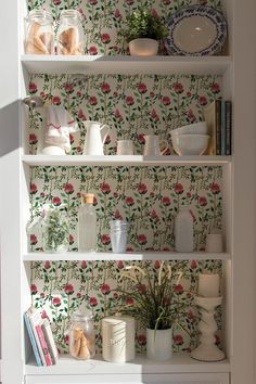 a white book shelf filled with vases and other items next to a wallpapered wall