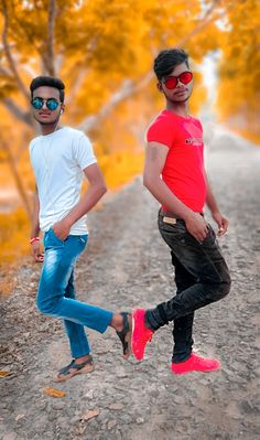 two young men are walking down a dirt road in front of trees with yellow leaves