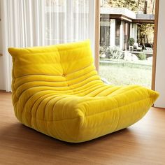 a large yellow bean bag chair sitting on top of a hard wood floor next to a window